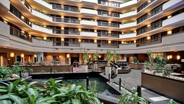 A multi-level hotel atrium with a central water feature, multiple balconies, and indoor plants. - Embassy Suites by Hilton Dulles Airport (Herndon)