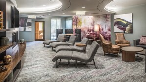 Eine moderne Hotelhalle mit gewölbter Decke, gemütlichen Sitzbereichen, einem Flachbildfernseher und einem großen abstrakten Gemälde an der Wand.