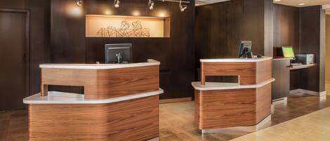 A reception area with two wooden reception desks, a wall-mounted artwork, and a computer on the right.