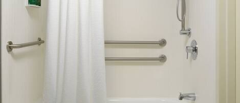A standard bathroom with a bathtub, grab bars, a showerhead, and a soap dispenser.