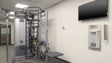 A gym with a weightlifting station, a hydration station, and a television mounted on the wall.