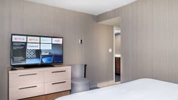Una habitación de hotel con una cama, un televisor en una cómoda y una puerta que da a otra estancia.