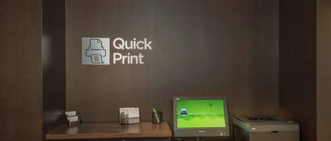 Un mostrador de recepción con un monitor que muestra un pase de abordar, una impresora y un letrero que dice 'Quick Print'.