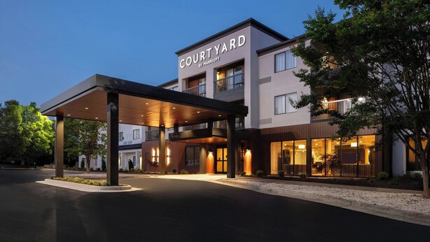 Ein Courtyard by Marriott Hotel mit überdachter Einfahrt, mehreren Etagen und einer gut beleuchteten Fassade.