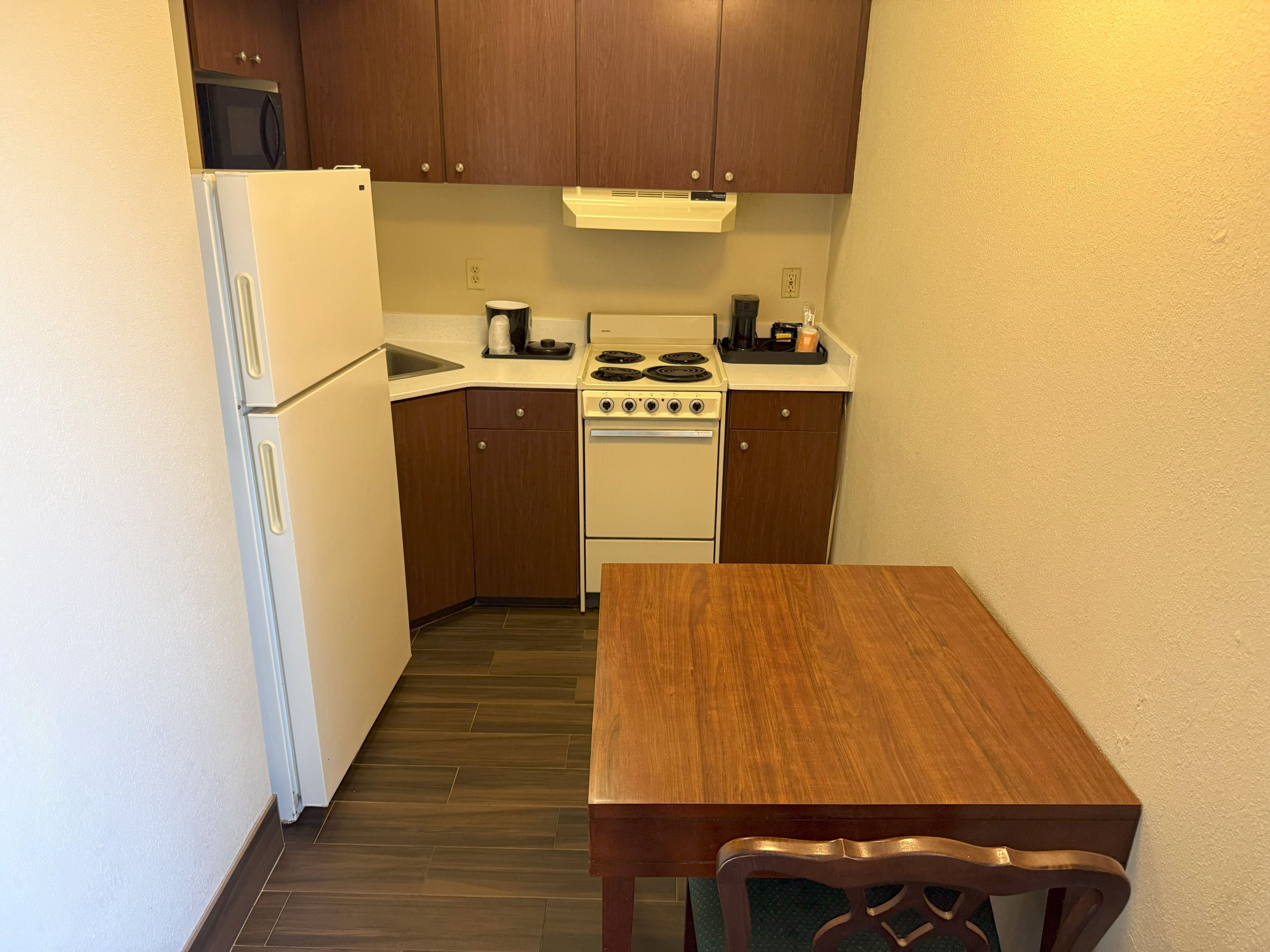 A compact kitchen with a refrigerator, stove, and wooden cabinets.