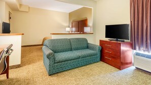 Una habitación de hotel con sofá, televisor, cómoda y espejo.
