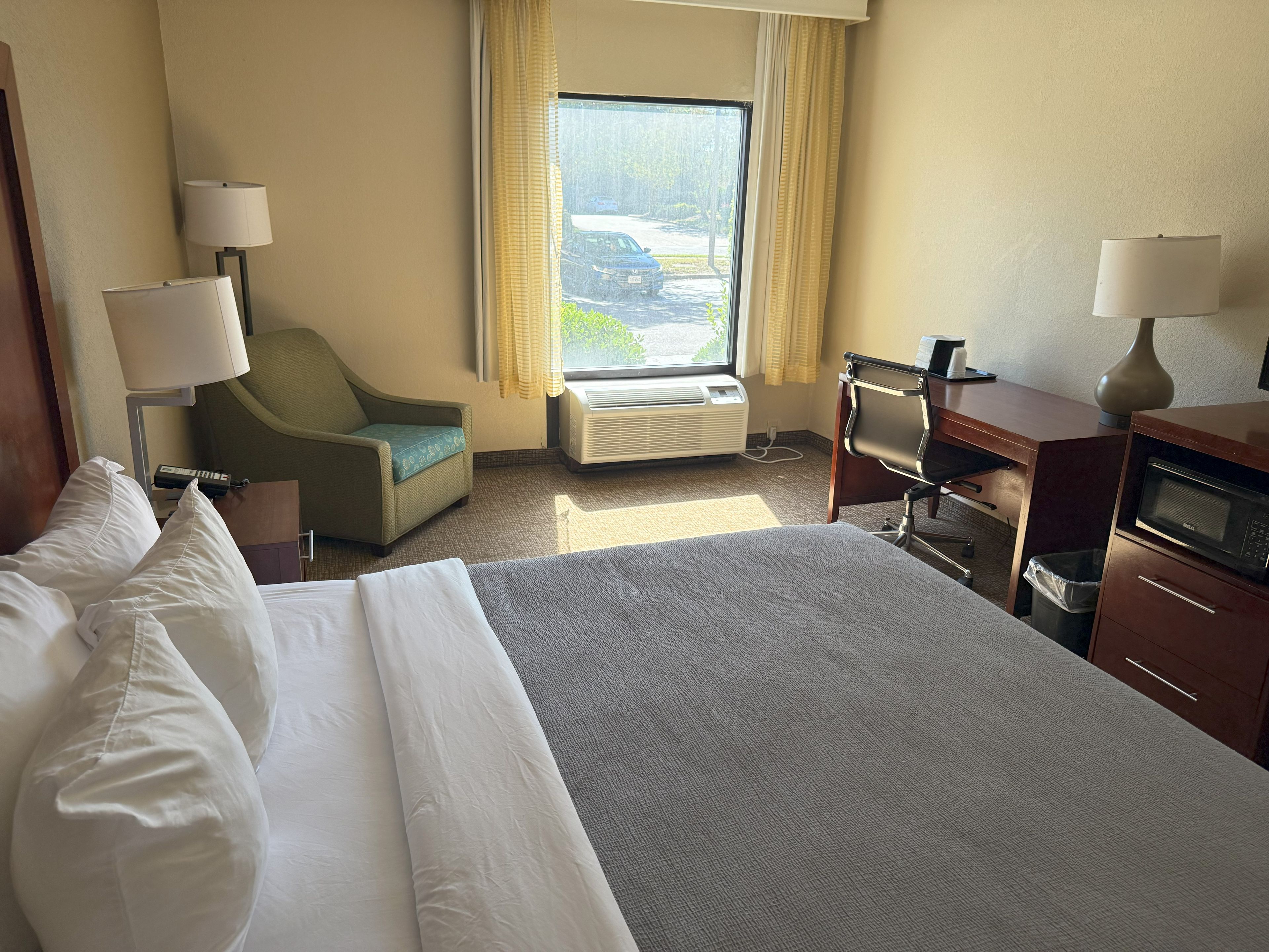 A hotel room with a bed, a desk, a chair, a lamp, and a window with curtains.