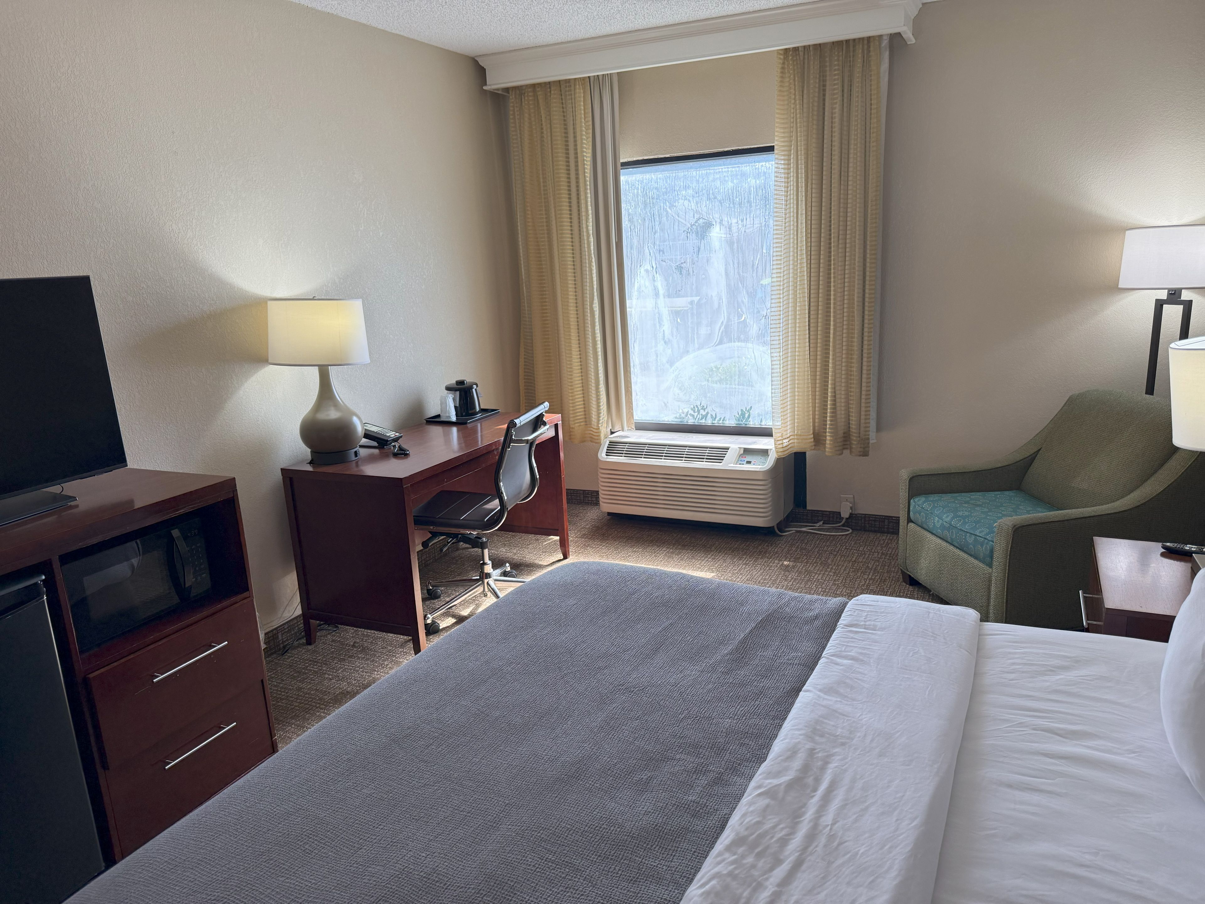A hotel room with a bed, desk, chair, television, and a window with curtains.