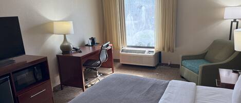 A hotel room with a bed, desk, chair, television, and a window with curtains.