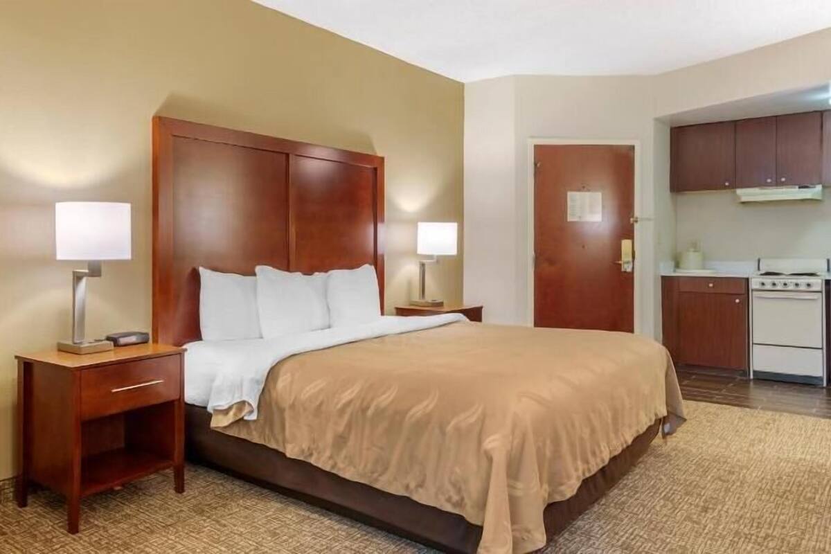 A hotel room with a bed, bedside tables, a lamp, a door, and a kitchenette.