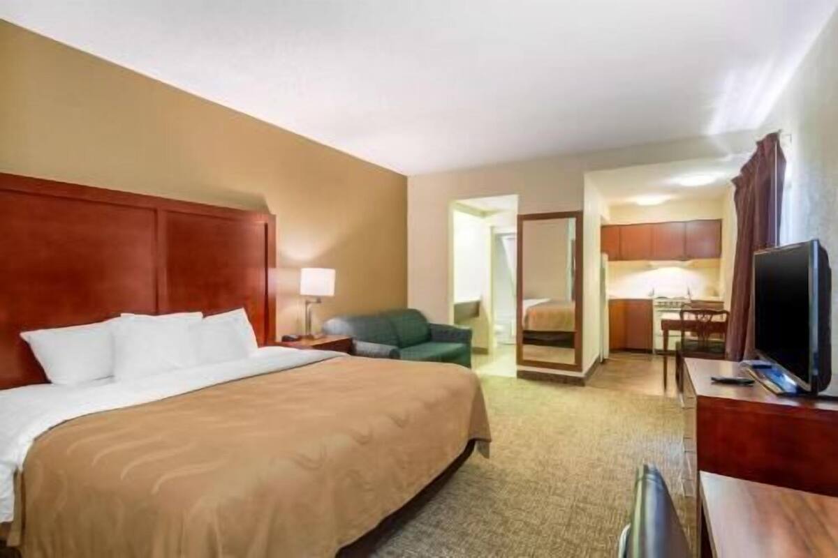 A hotel room with a bed, a desk, a television, and a kitchenette.