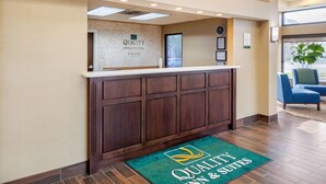 Un área de recepción con un mostrador de madera, un reloj y una alfombra verde con el logotipo del hotel.