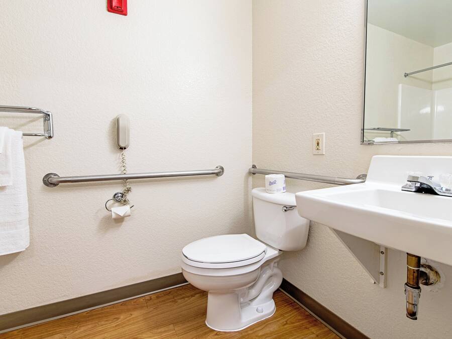 A bathroom with a white toilet, a sink, a mirror, a towel rack, and a handrail.