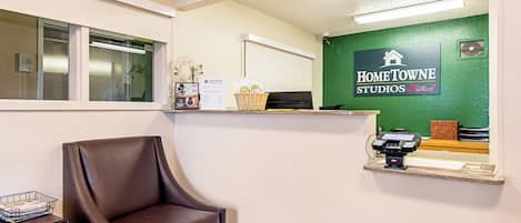 A reception area with a brown leather chair, a reception desk, a green wall with a sign, and a window with blinds.