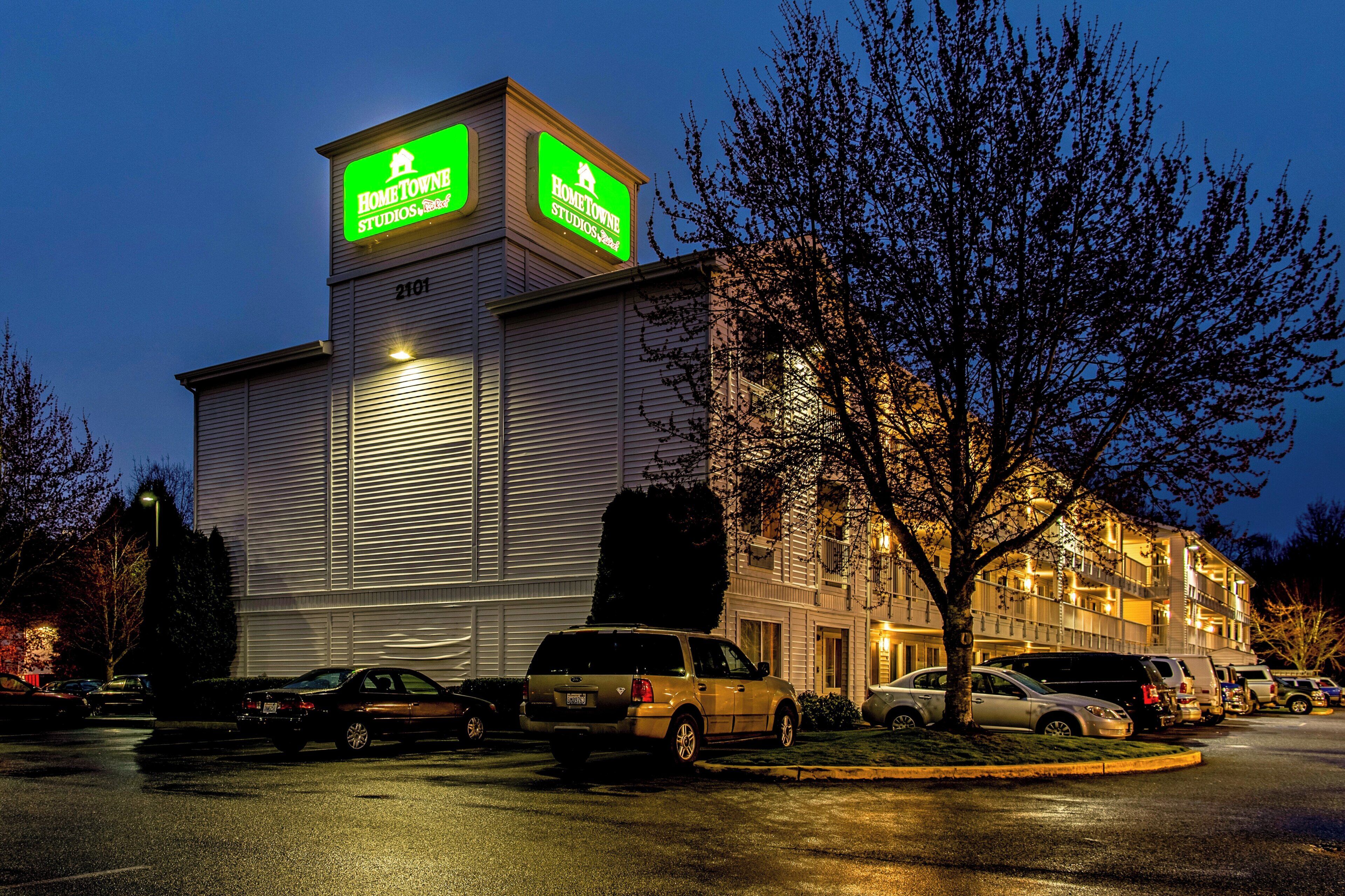 Un bâtiment portant une enseigne « HomeTown Studios » et un parking où sont garées plusieurs voitures.