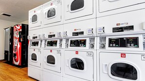 A row of white front-loading washing machines with control panels, arranged in a commercial setting. - HomeTowne Studios by Red Roof Tacoma - Puyallup (Puyallup)