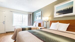 A hotel room with two beds, a large window, a painting on the wall, and a nightstand with a lamp. - HomeTowne Studios by Red Roof Tacoma - Puyallup (Puyallup)