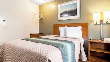 A hotel room with a bed, a nightstand, a lamp, a painting, and a coat rack.