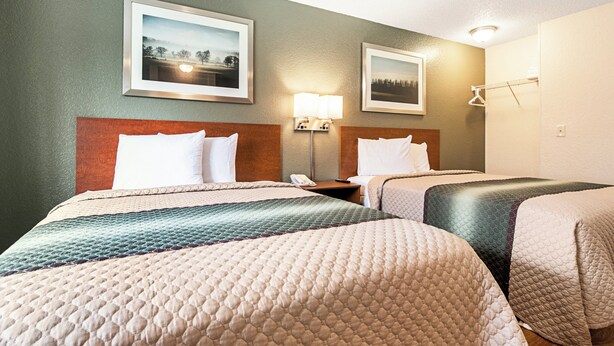 A hotel room with two beds, a nightstand, a lamp, and two framed pictures on the wall. - HomeTowne Studios by Red Roof Tacoma - Puyallup (Puyallup)