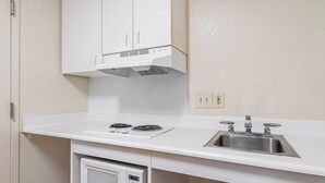A kitchen with a microwave, stove, sink, and white cabinets. - HomeTowne Studios by Red Roof Tacoma - Puyallup (Puyallup)