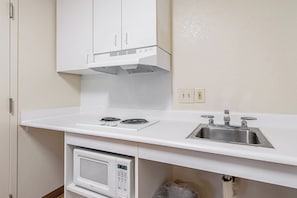 A kitchen with a microwave, stove, sink, and white cabinets. - HomeTowne Studios by Red Roof Tacoma - Puyallup (Puyallup)