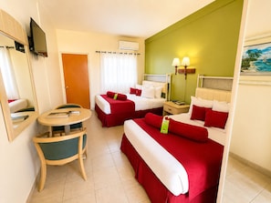 Habitación de hotel con dos camas, un escritorio, una silla, televisión, ventana con cortinas y un cuadro en la pared.