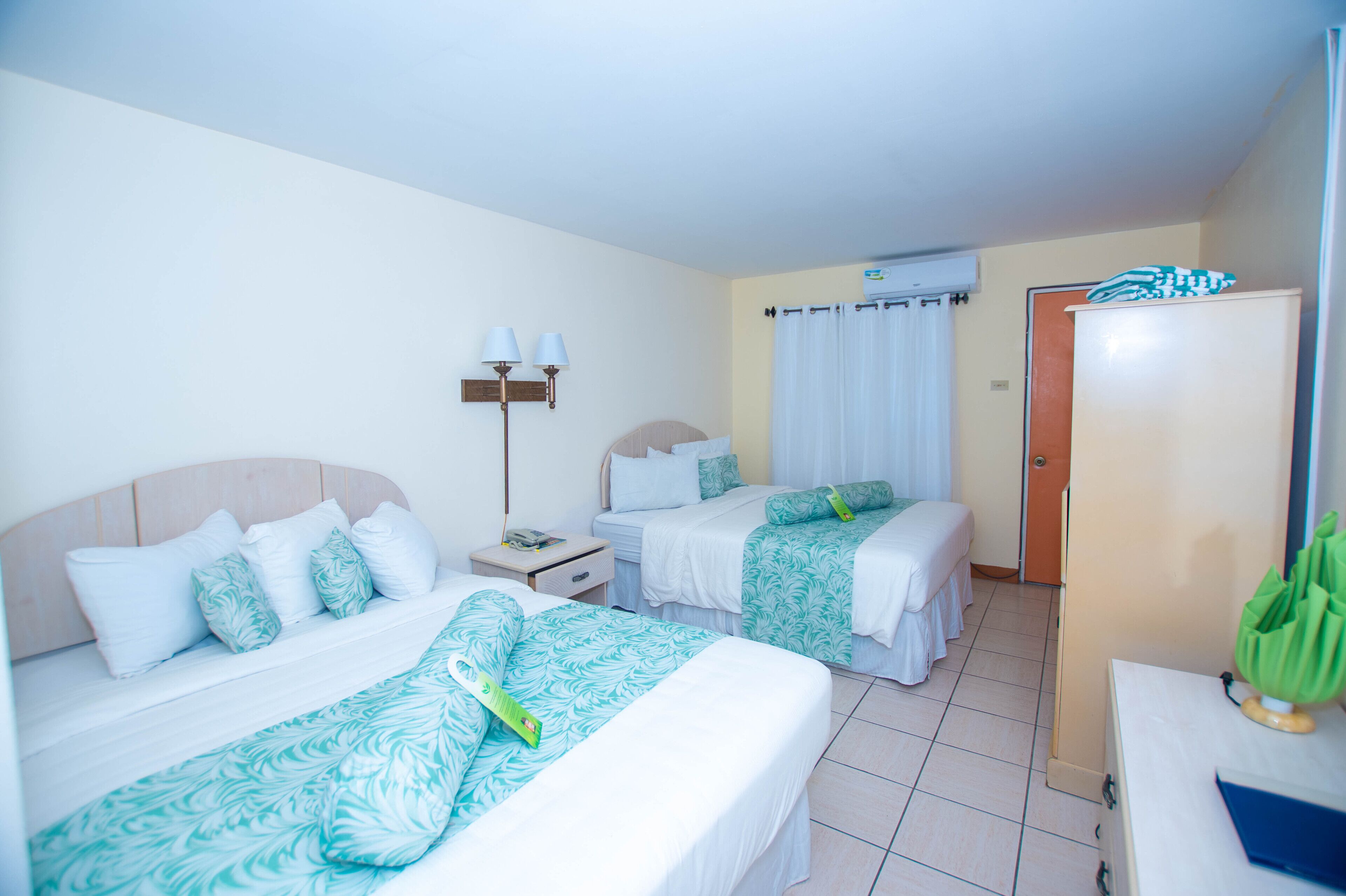 A hotel room with two beds, a nightstand, a lamp, a wardrobe, and a bathroom with a curtain.