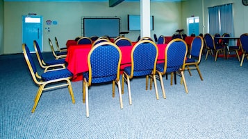 Un salón de conferencias con una larga mesa, sillas azules y un mantel rojo.