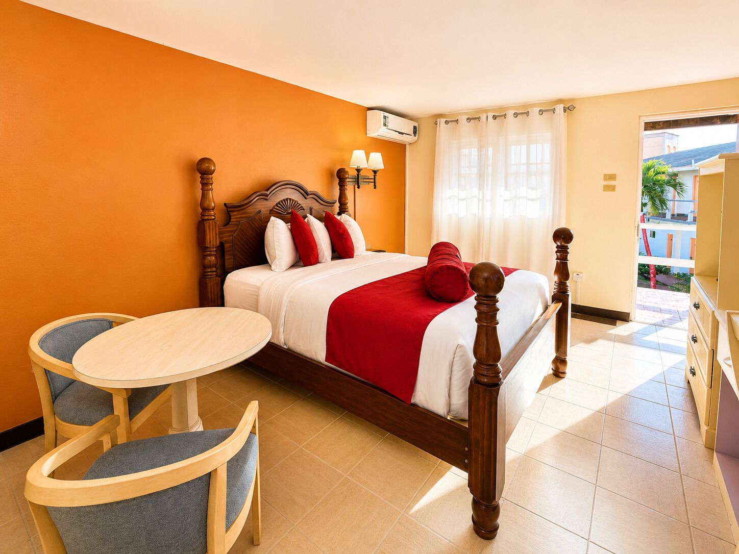 A hotel room with a bed, a small round table, two chairs, a window with curtains, and an air conditioning unit.