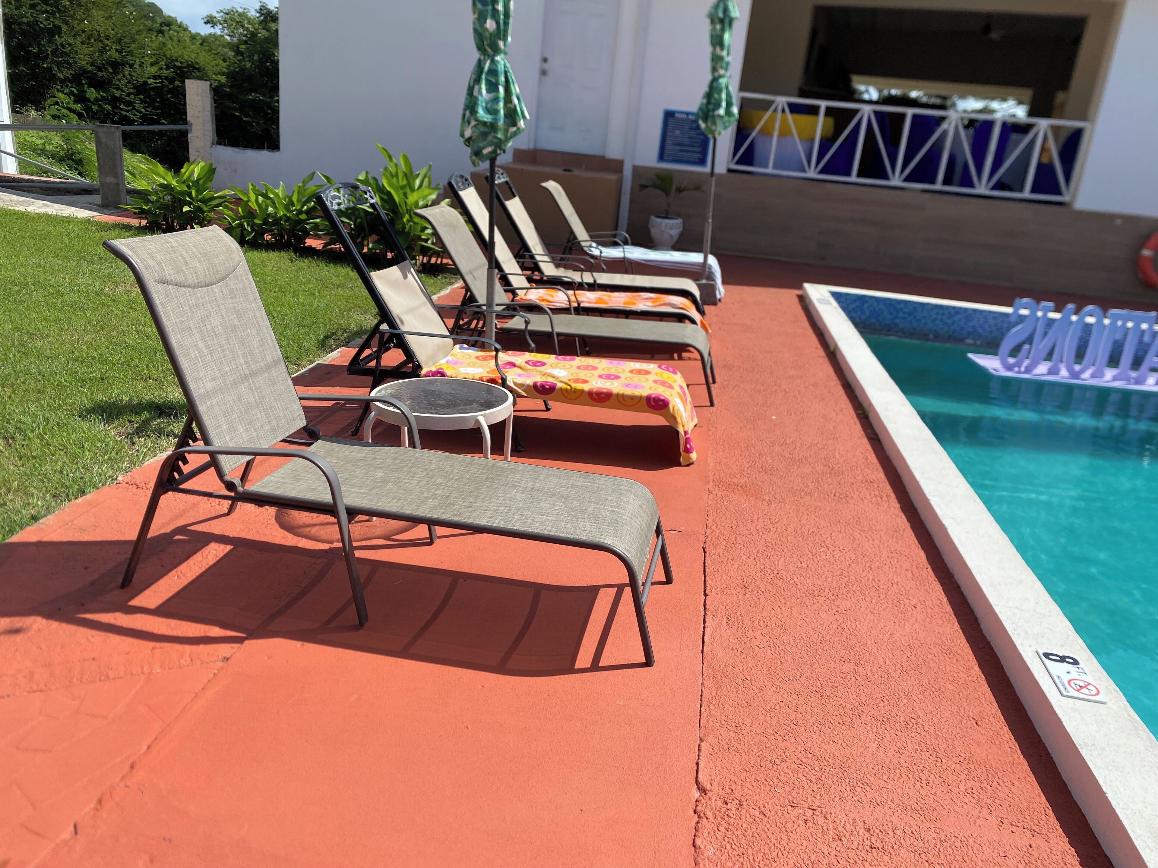 Ein Poolbereich mit Liegestühlen und Sonnenschirmen, einem Schwimmbecken und einem weißen Gebäude im Hintergrund.