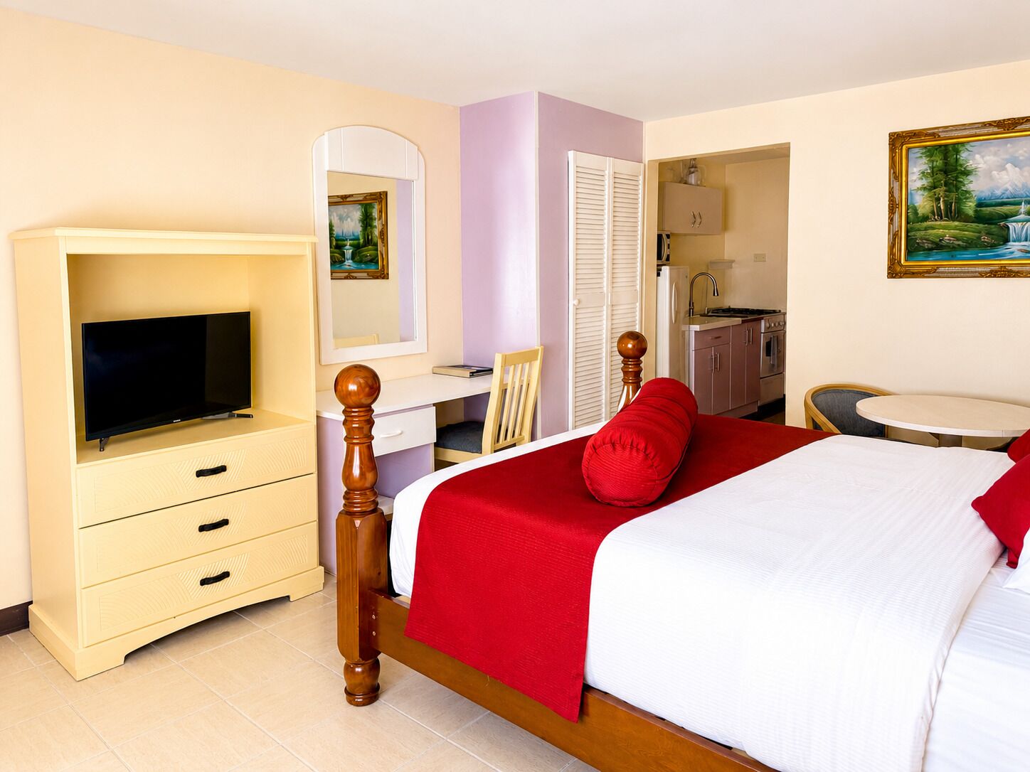 Quarto de hotel com cama, televisão, escrivaninha, cadeira, mesinha e um quadro na parede.