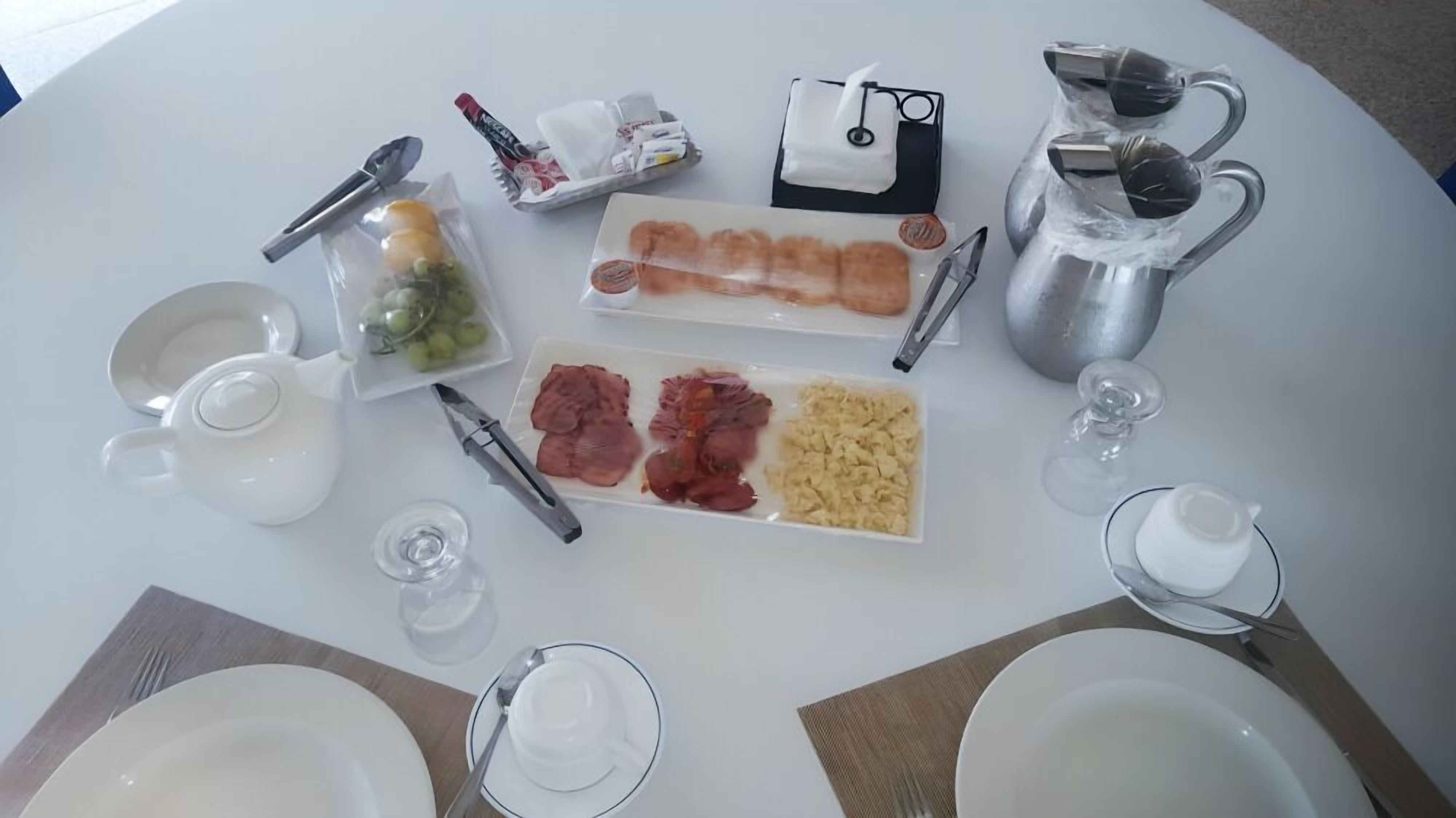 A table set for breakfast with plates of food, a coffee pot, and various utensils.