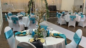 Une salle de banquet avec des tables rondes, des chaises blanches ornées de rubans turquoise et un arrangement floral central.