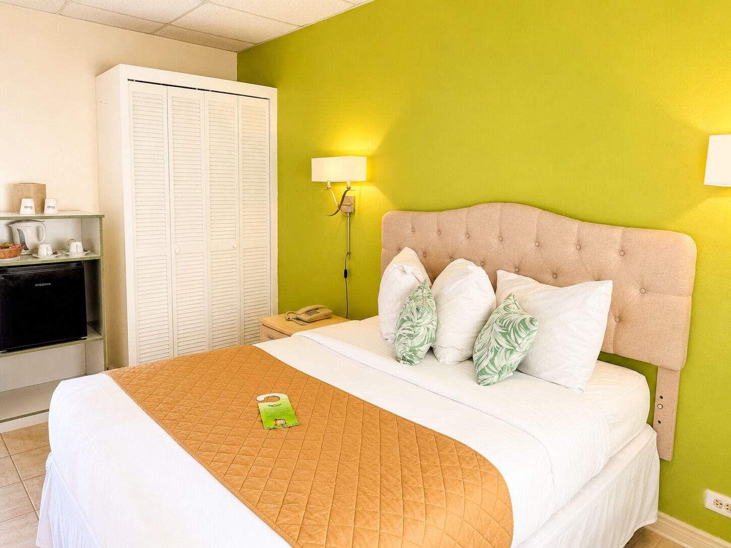A hotel room with a bed, a nightstand with a phone, a wardrobe, and a kitchenette.