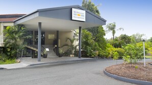 A hotel entrance with a covered walkway, outdoor seating, and a sign indicating "Mt Ommaney Hotel Apartments."