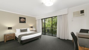 A hotel room with a large bed, a desk, a chair, a nightstand, a lamp, a picture on the wall, and a window with curtains.