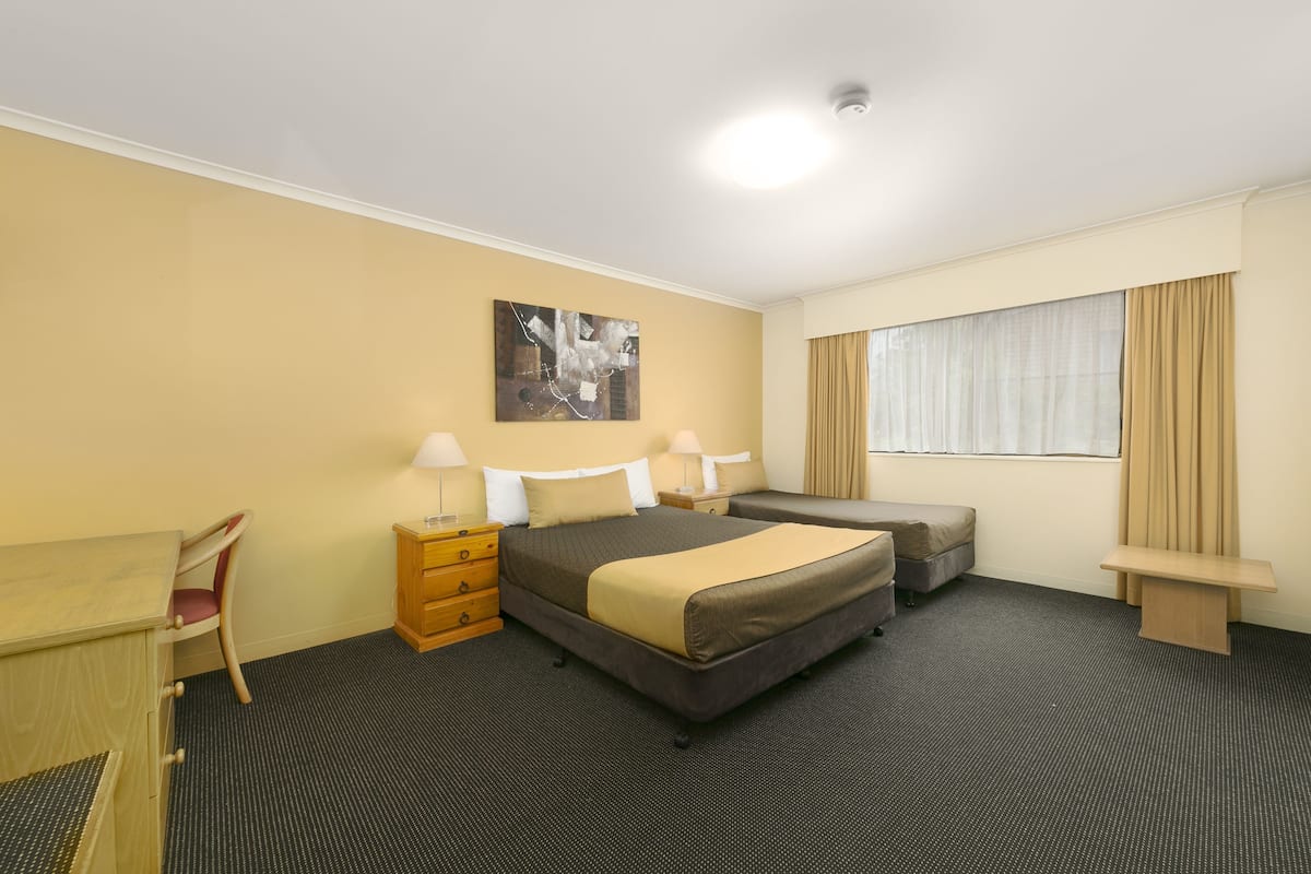 Een hotelkamer met een bed, een bureau, een stoel, een dressoir en een raam met gordijnen.