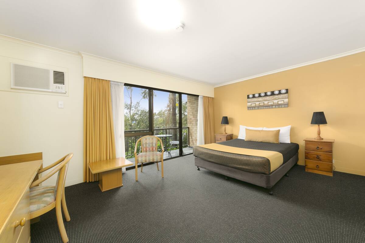 Hotelkamer met een bed, bureau, stoel, klein tafeltje, balkon met gordijnen en plafondventilator.