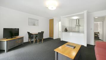 A modern hotel room with a flat-screen TV, a wooden desk, a red sofa, and a kitchenette.