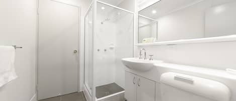 Un baño moderno con ducha de vidrio, lavamanos blanco y un espejo grande.