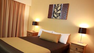 A hotel room with a large bed, two bedside tables, a nightstand, and a wall-mounted artwork.