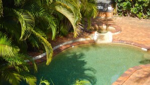 A swimming pool surrounded by a brick walkway and lush greenery.