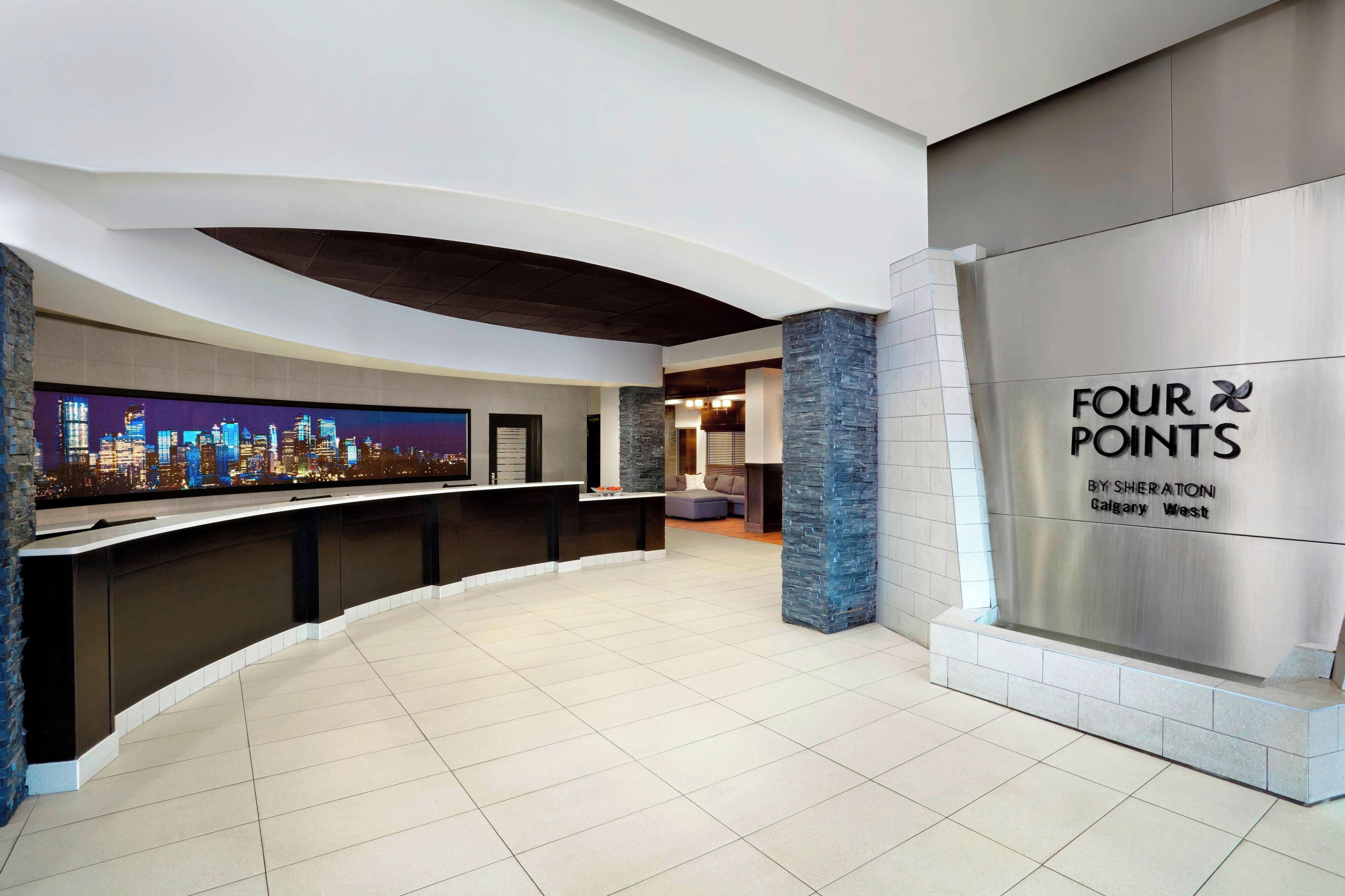 A modern lobby with a curved reception desk, a large digital cityscape display, and a prominent 'FOUR POINTS' sign.
