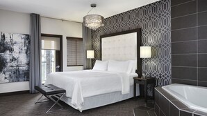 Una habitación de hotel moderna con una cama grande, un banco para sentarse, una bañera y un candelabro.