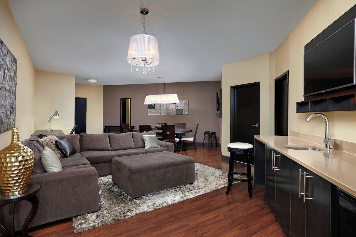 Una sala moderna con un sofá seccional, una zona de comedor y una cocina con un televisor grande.