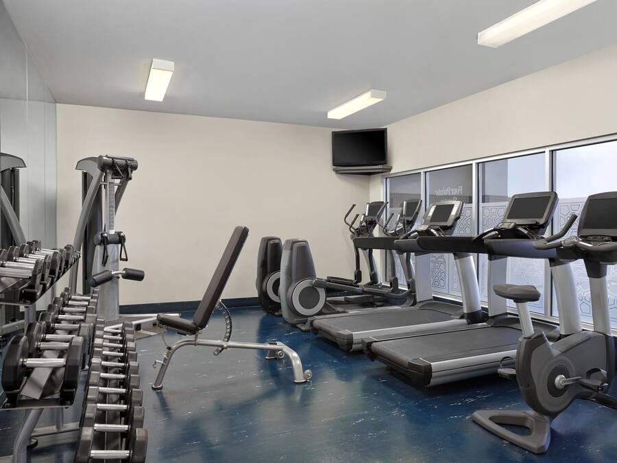 Un gimnasio con equipo de ejercicio variado, incluyendo cintas de correr, elípticas y máquinas de pesas.
