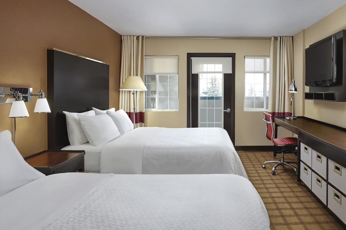 A hotel room with two beds, a desk, a chair, a TV, and a window.