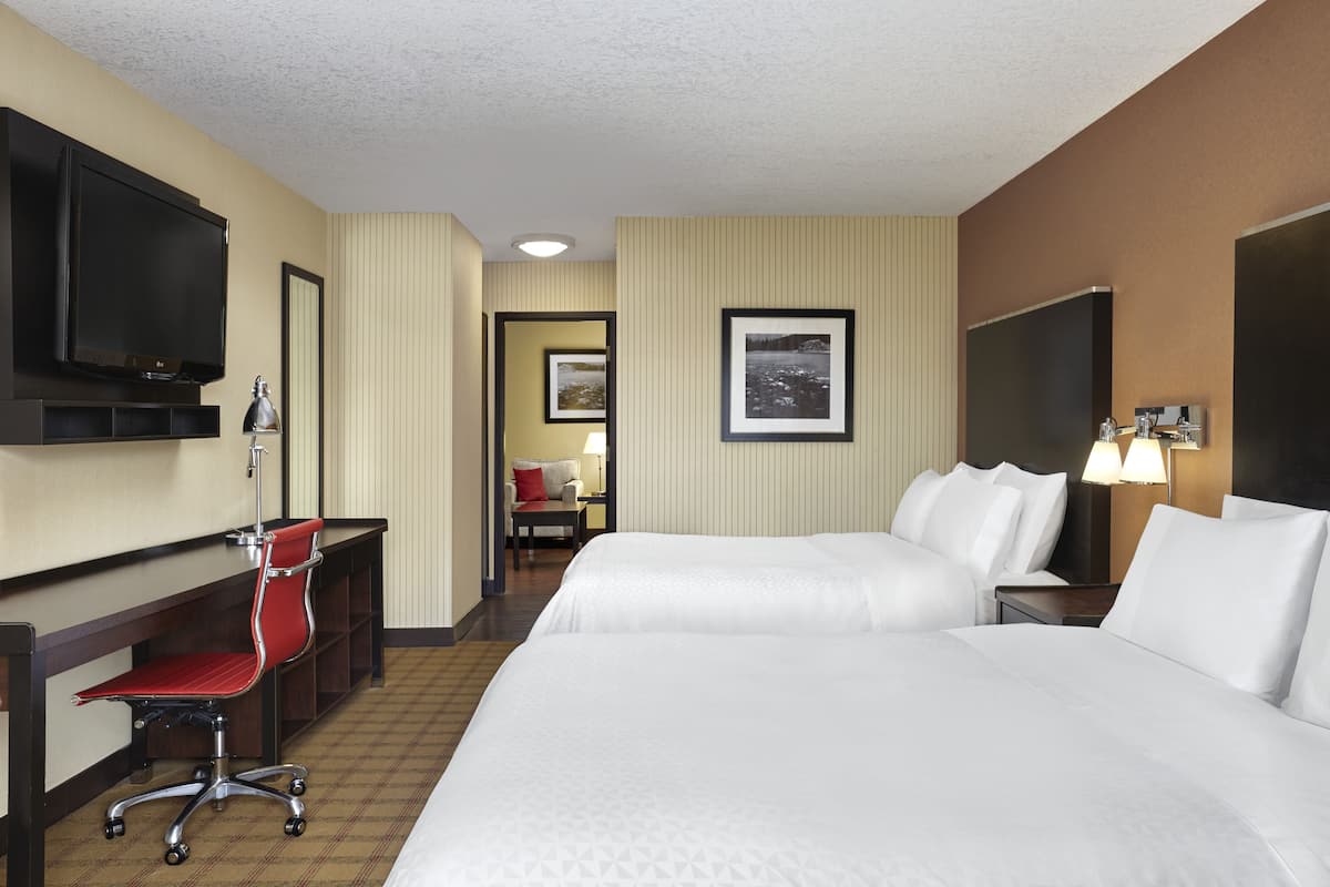 A hotel room with two beds, a desk with a chair, a television, and a framed picture on the wall.