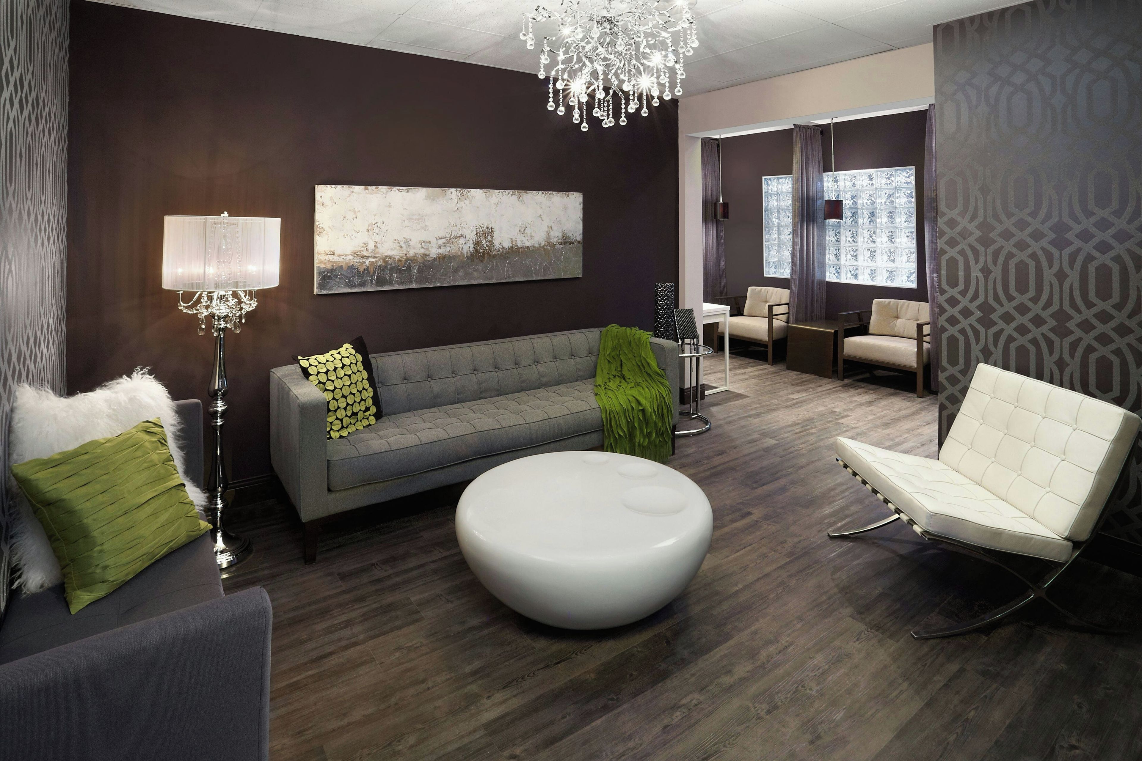 Een moderne woonkamer met een grijze bank, een witte voetenbank, een witte fauteuil en een kroonluchter.
