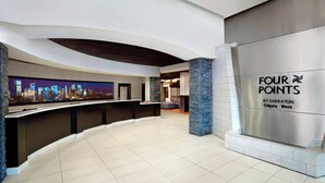 Un vestíbulo moderno con un mostrador de recepción curvo, una pantalla con vistas a la ciudad y un cartel de 'Four Points by Sheraton Calgary West'.